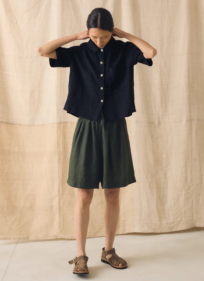 Woman wearing a black top and green shorts against a beige curtain background