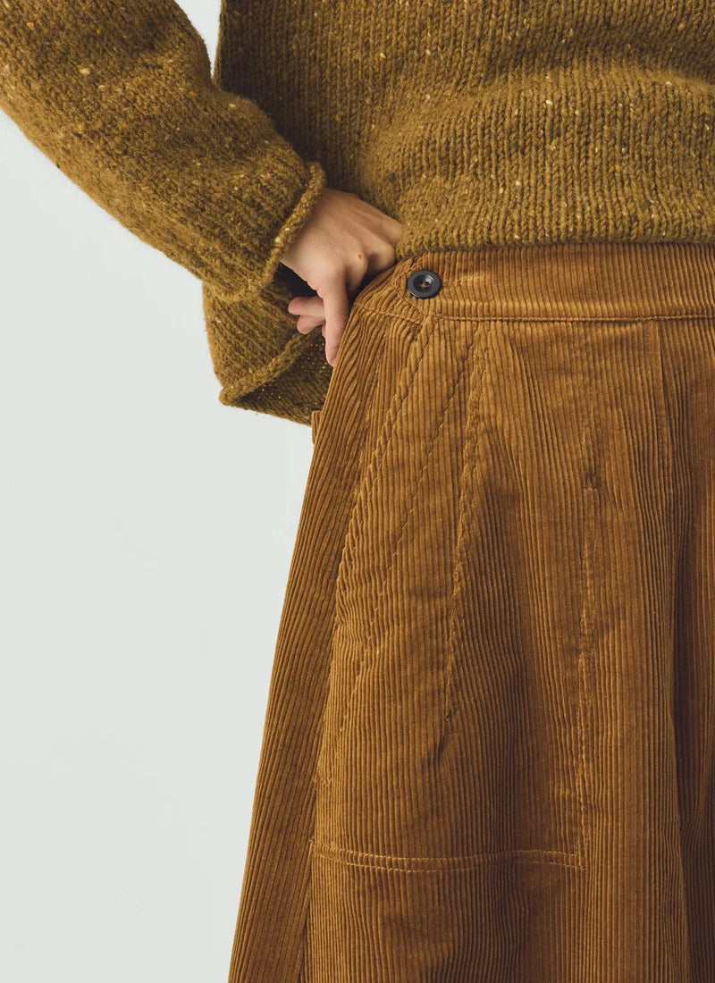 A closeup detail of a model wearing a soft brown sweater and a golden amber corduroy skirt.