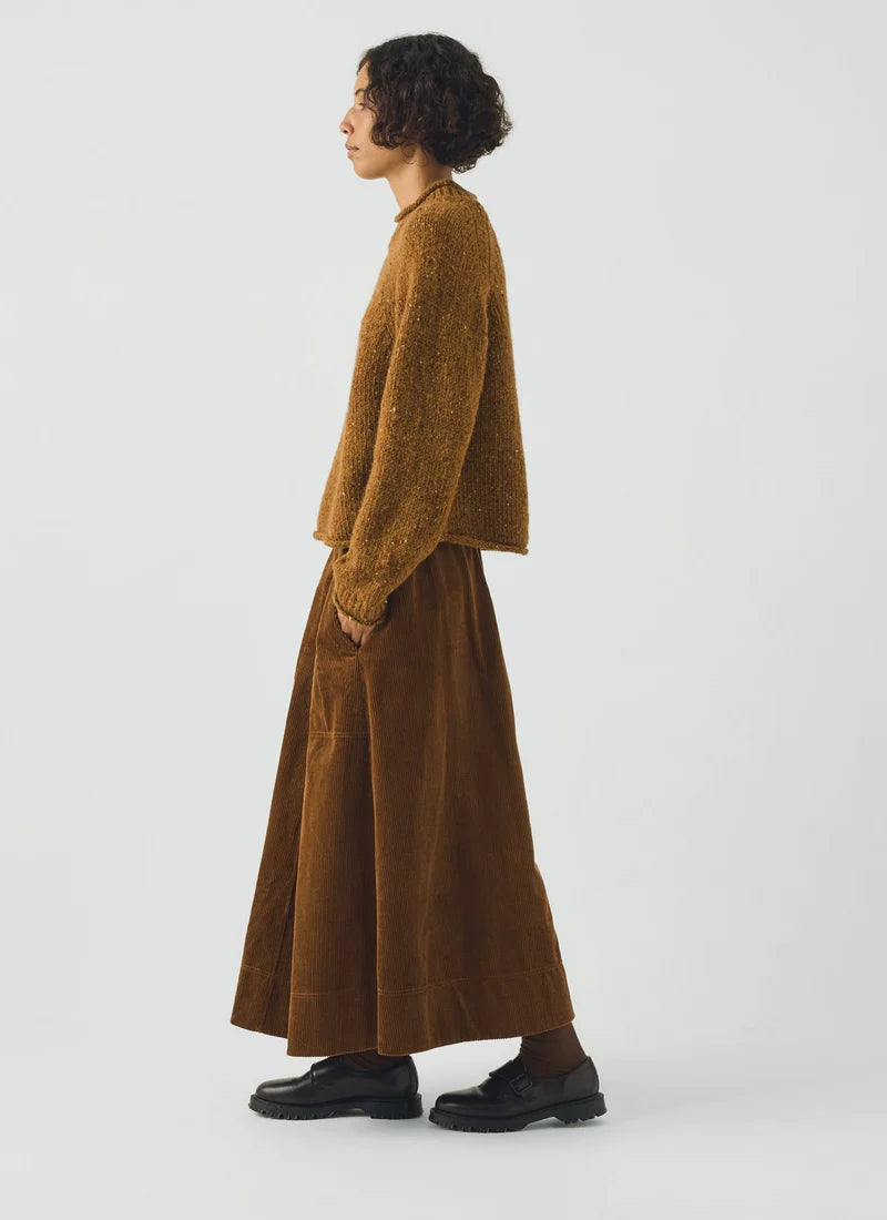 Person wearing a brown corduroy skirt showing the ribbed texture, a dark button, and part of a fuzzy brown collar against a light gray background.