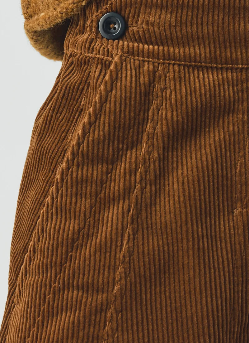 Close-up of a brown corduroy garment, likely a skirt or pants, showing the ribbed texture, a dark button, and part of a fuzzy brown collar against a light gray background.