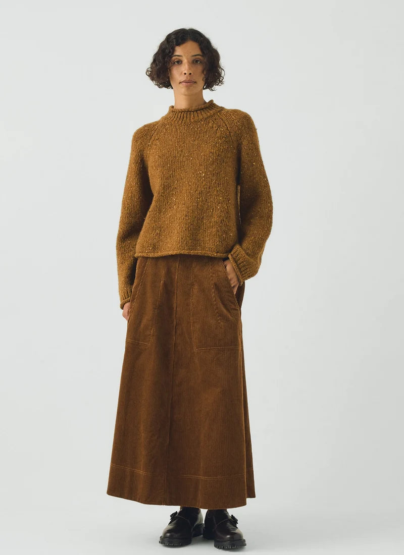 Woman wearing a brown corduroy skirt showing the ribbed texture, a dark button, and part of a fuzzy brown collar against a light gray background.