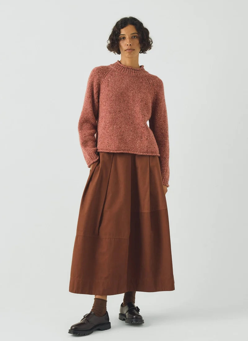 Woman wearing a coral colored sweater and brown skirt.