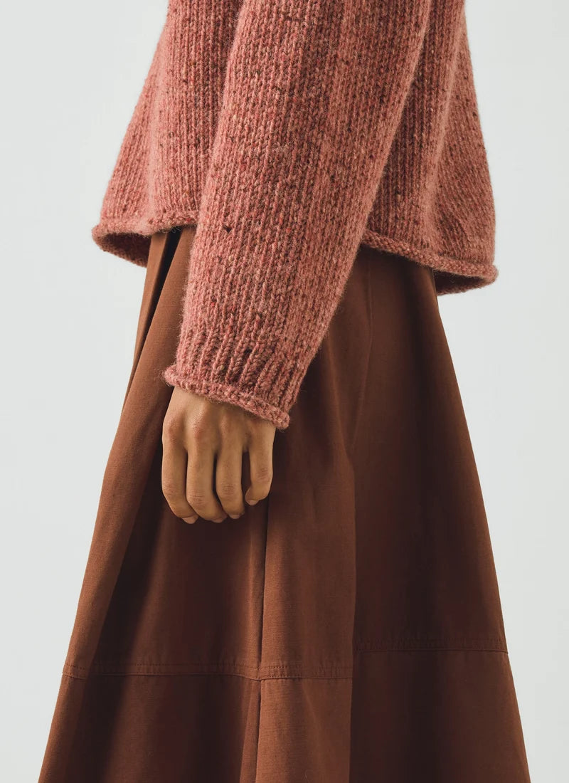 Close up detail of woman wearing a coral colored sweater and brown skirt.