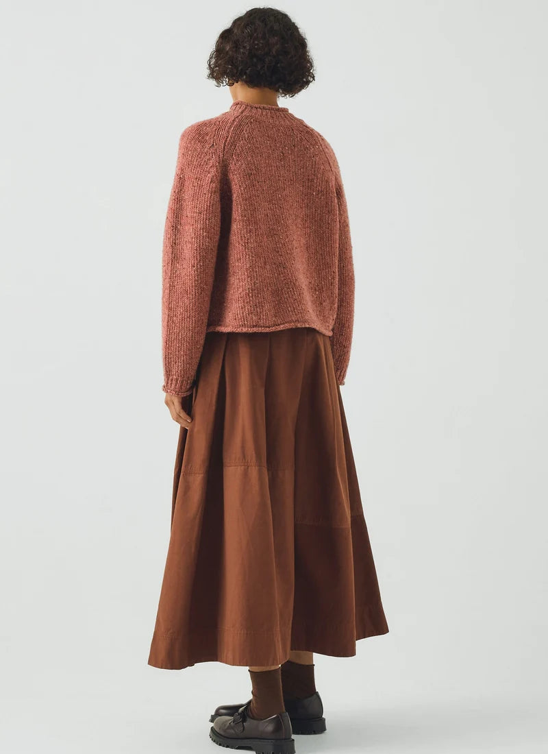 Woman wearing a coral colored sweater and brown skirt, reverse view