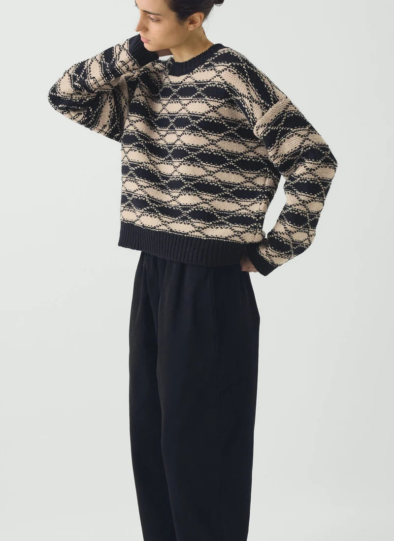 Side view of person wearing blue pants and striped blue and white jacquard sweater against a grey background.