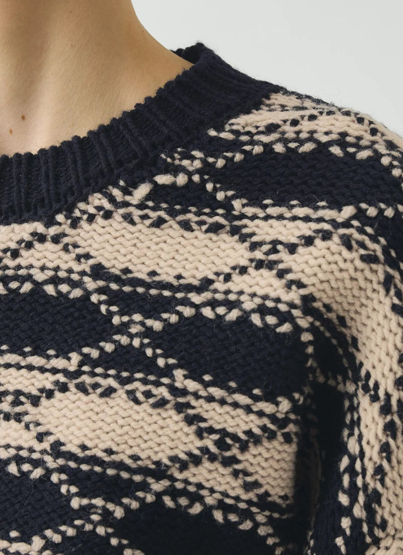 Close up view of person wearing blue pants and striped blue and white jacquard sweater against a grey background.