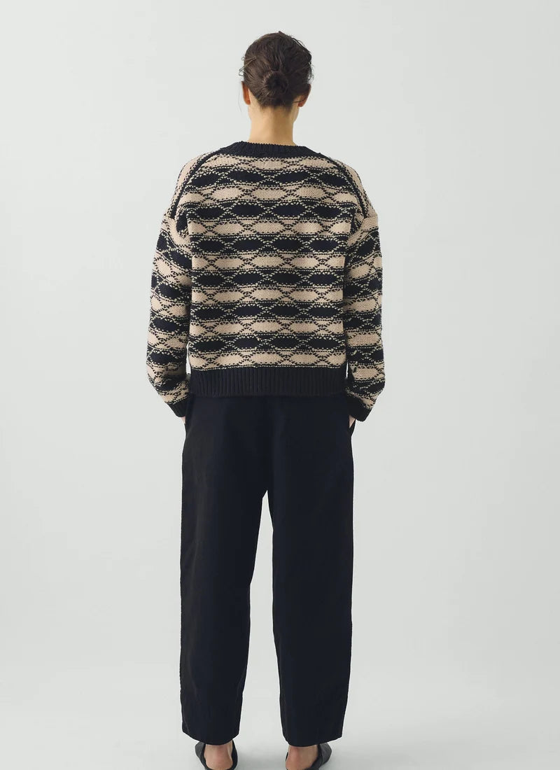 Rear view of person wearing blue pants and striped blue and white jacquard sweater against a grey background.
