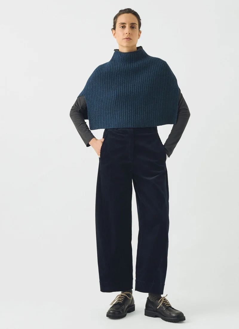 Woman wearing blue pants with a blue knitted poncho against a gret background