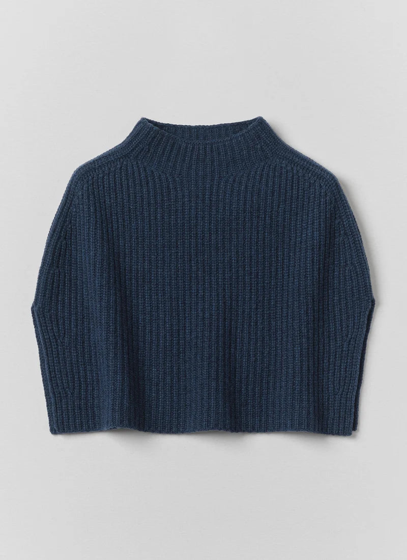 A blue knitted poncho against a grey background