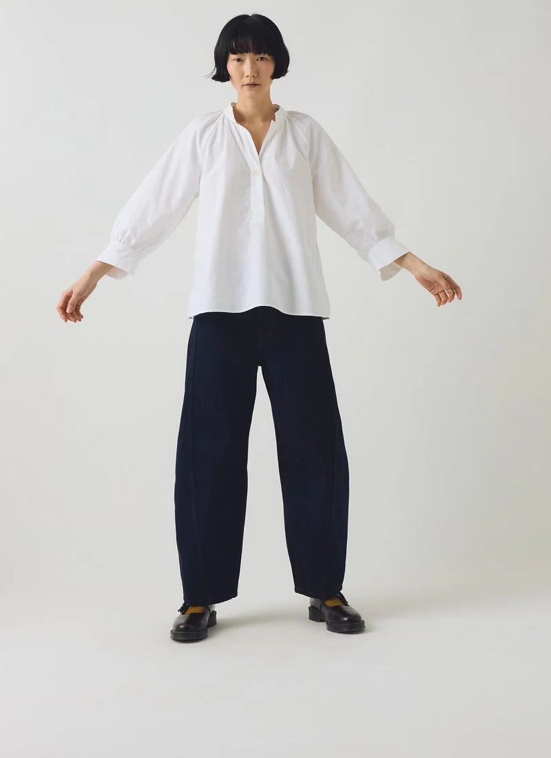 A model shown posing with a white cotton oxford shirt and dark navy barrel trousers.