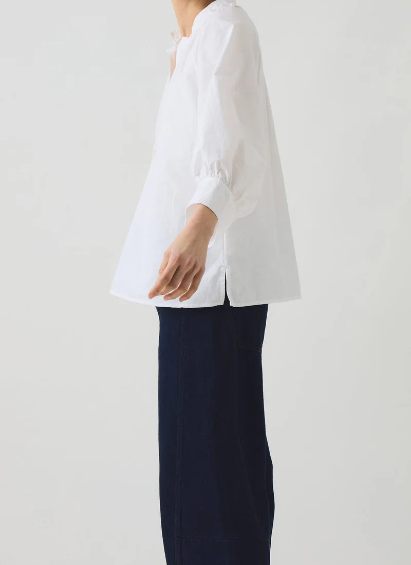 A model shown posing with a white cotton oxford shirt and dark navy barrel trousers.