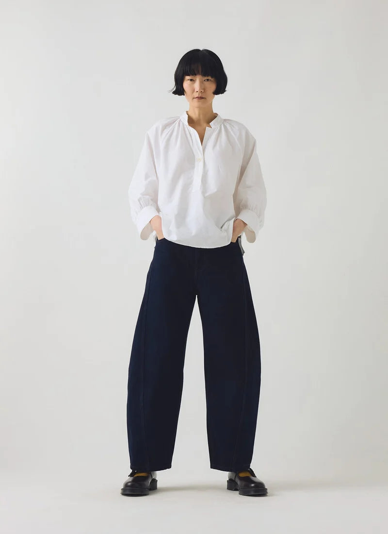 A model shown posing with a white cotton oxford shirt and dark navy barrel trousers.