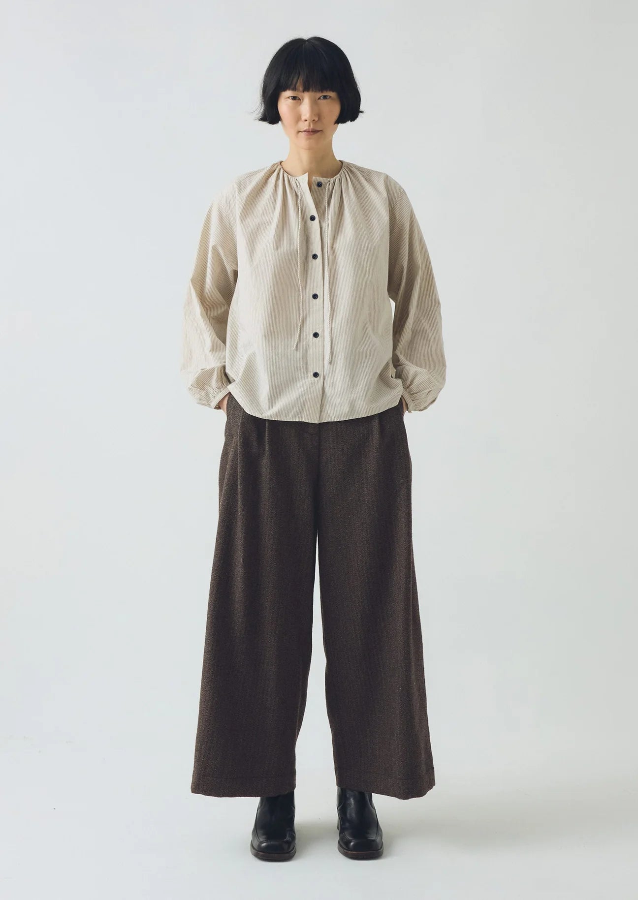 Person wearing a beige shirt and brown pants on a white background