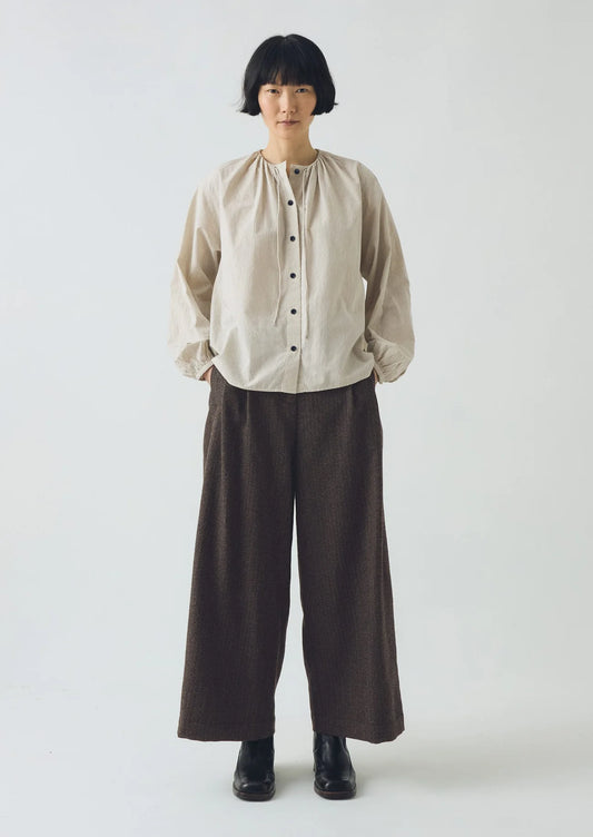 Person wearing a beige shirt and brown pants on a white background