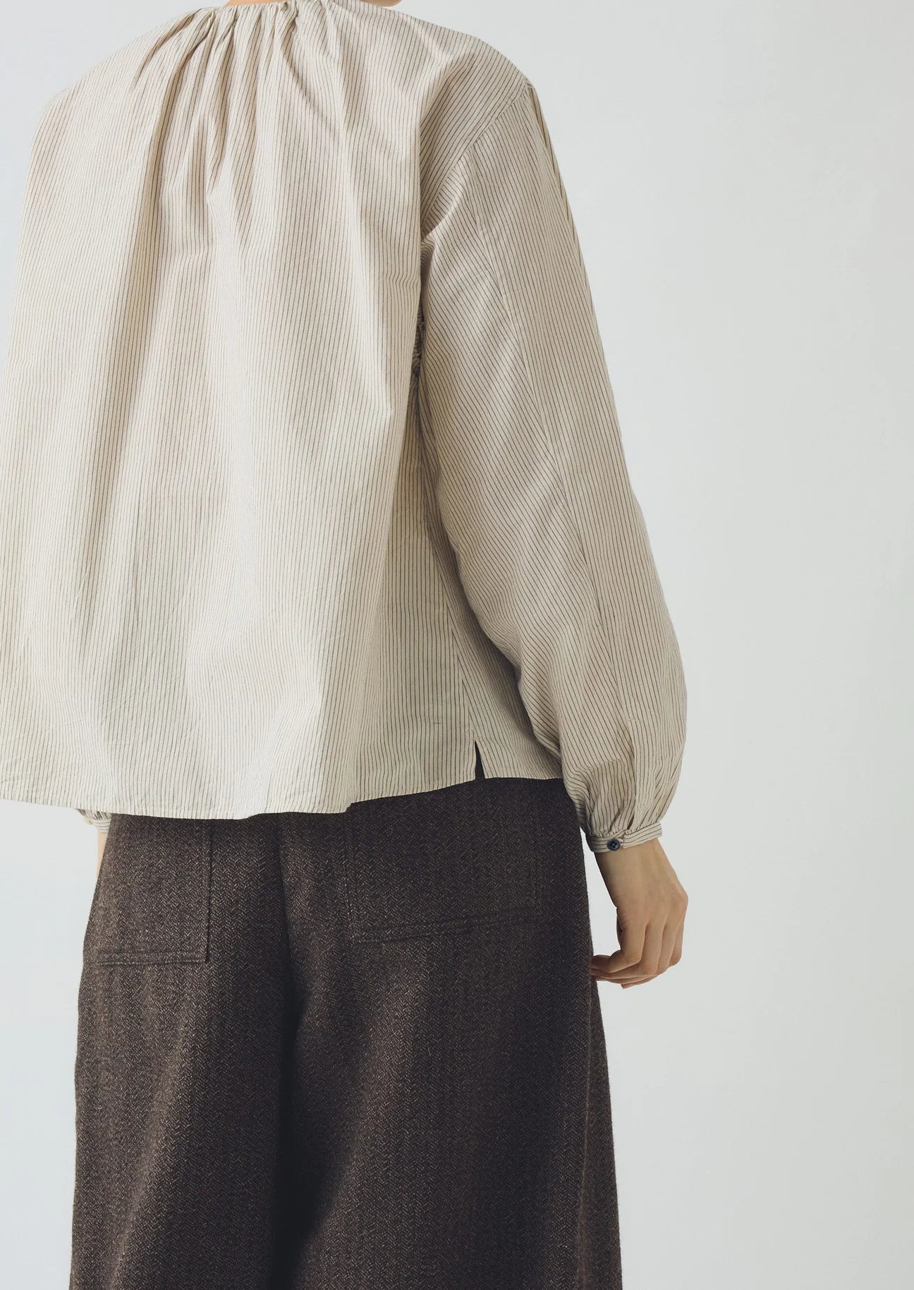 Person wearing a beige textured blouse and brown pants against a white background
