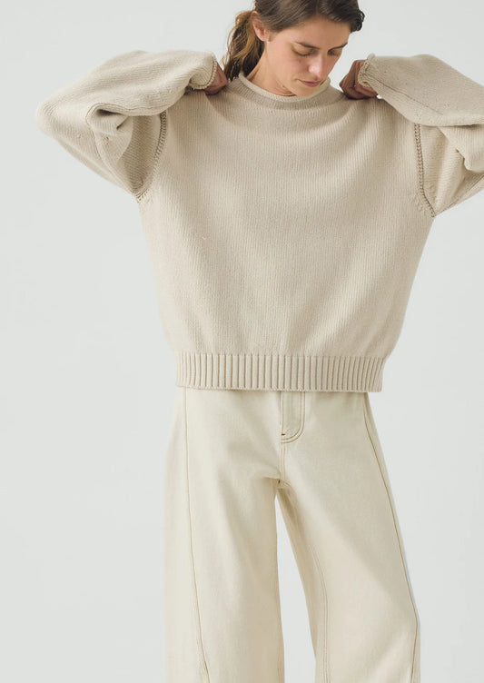 Woman wearing a beige sweater and pants on a light gray background