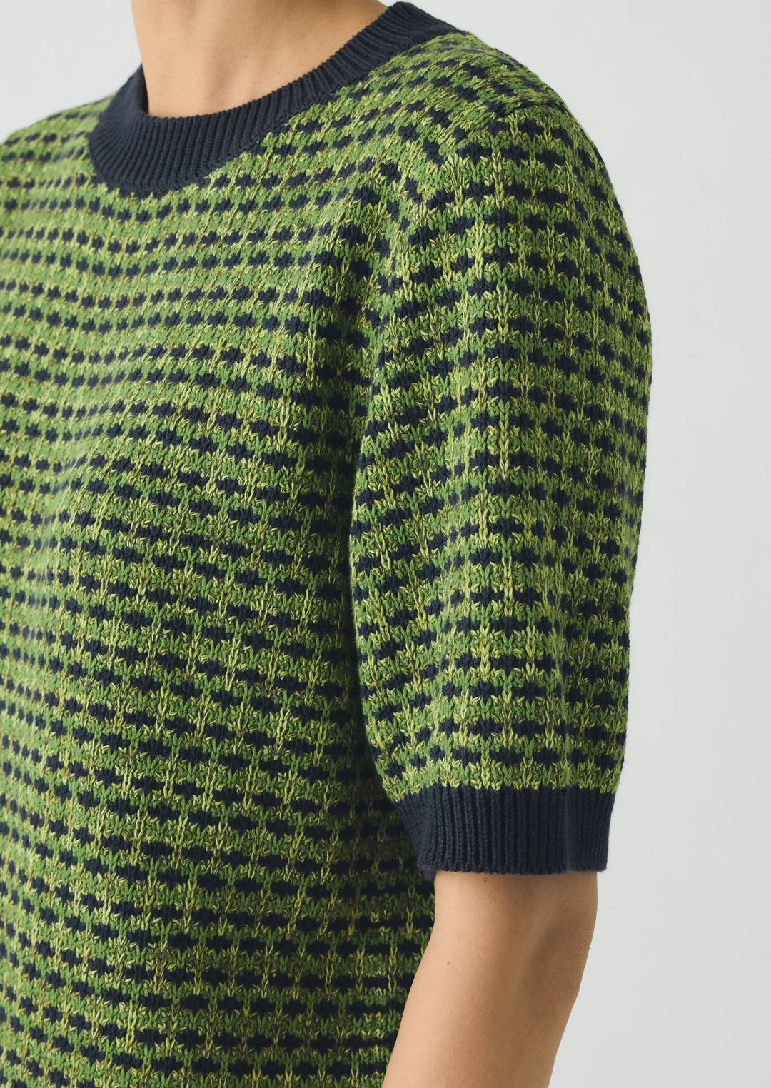Green and navy patterned sweater on a neutral background