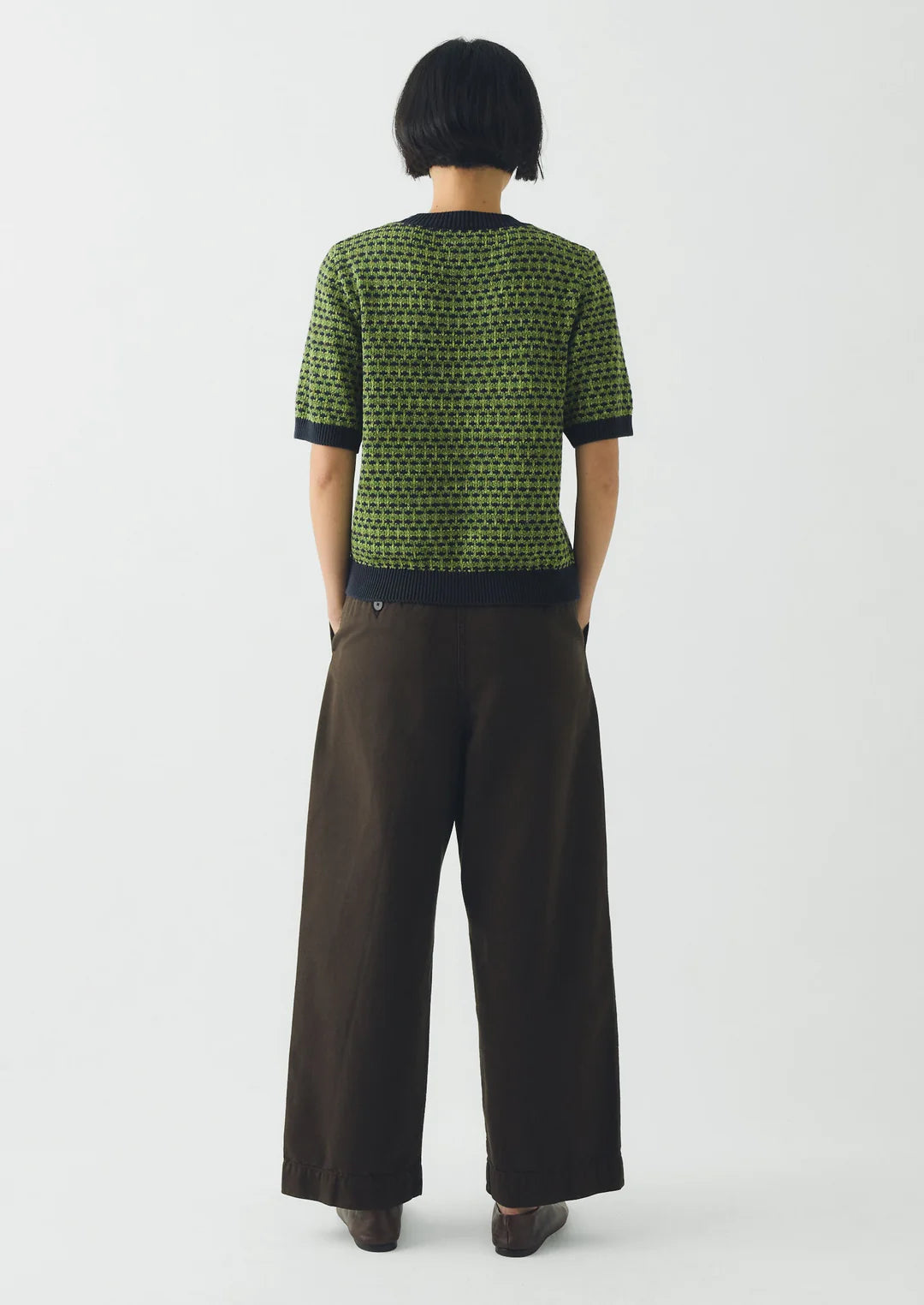 Person wearing a green and black patterned top with brown wide-leg pants on a white background