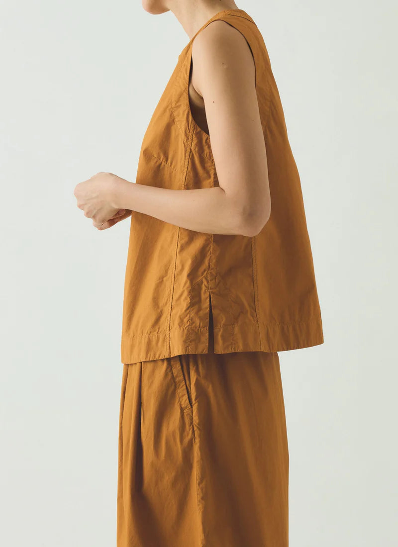 Person wearing a mustard yellow sleeveless top and pants on a plain background