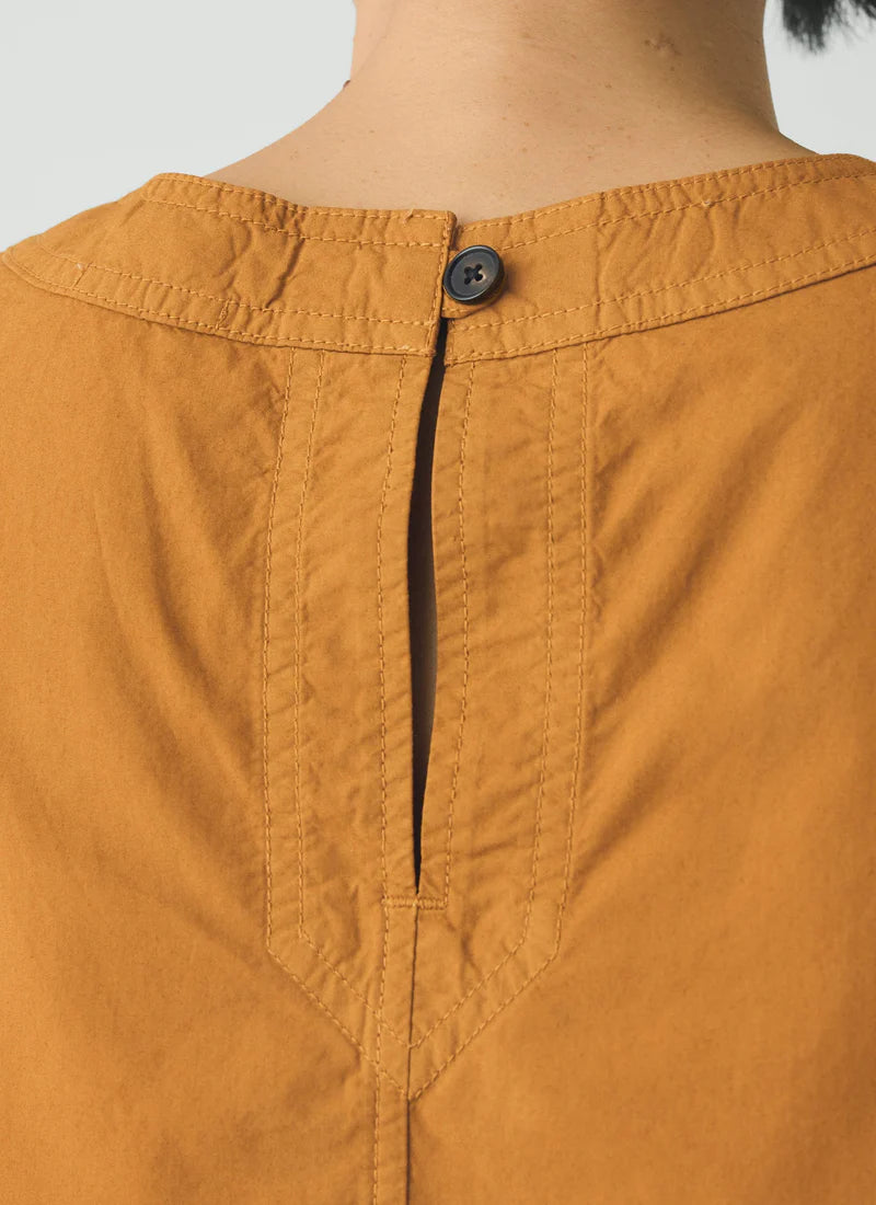 Detail of button closure on person wearing a mustard yellow sleeveless top 
