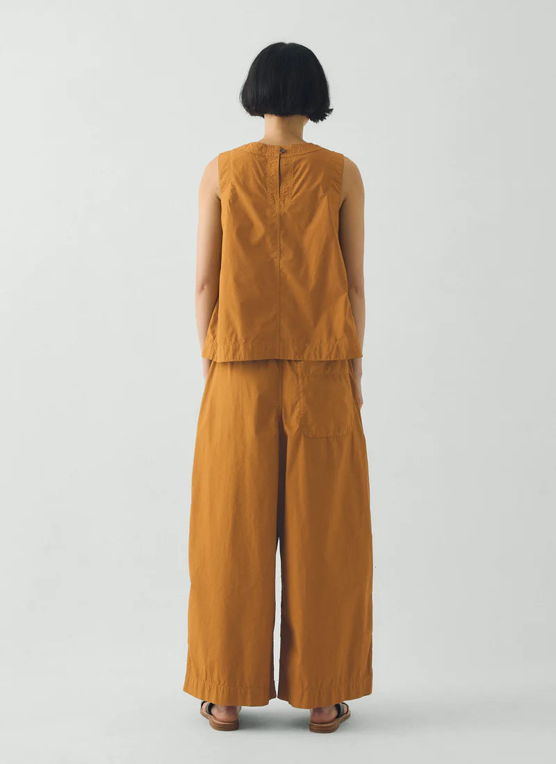 Person wearing a mustard yellow sleeveless top and pants on a plain background
