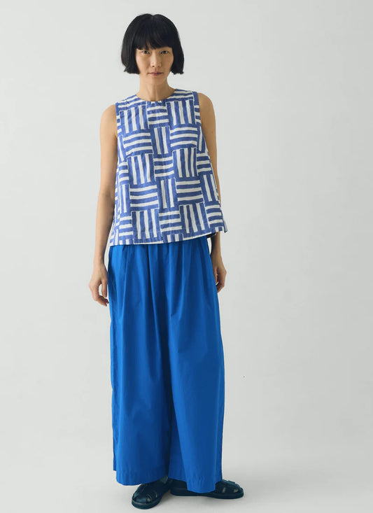 Woman wearing a blue and white patterned sleeveless top with a long blue skirt on a white background