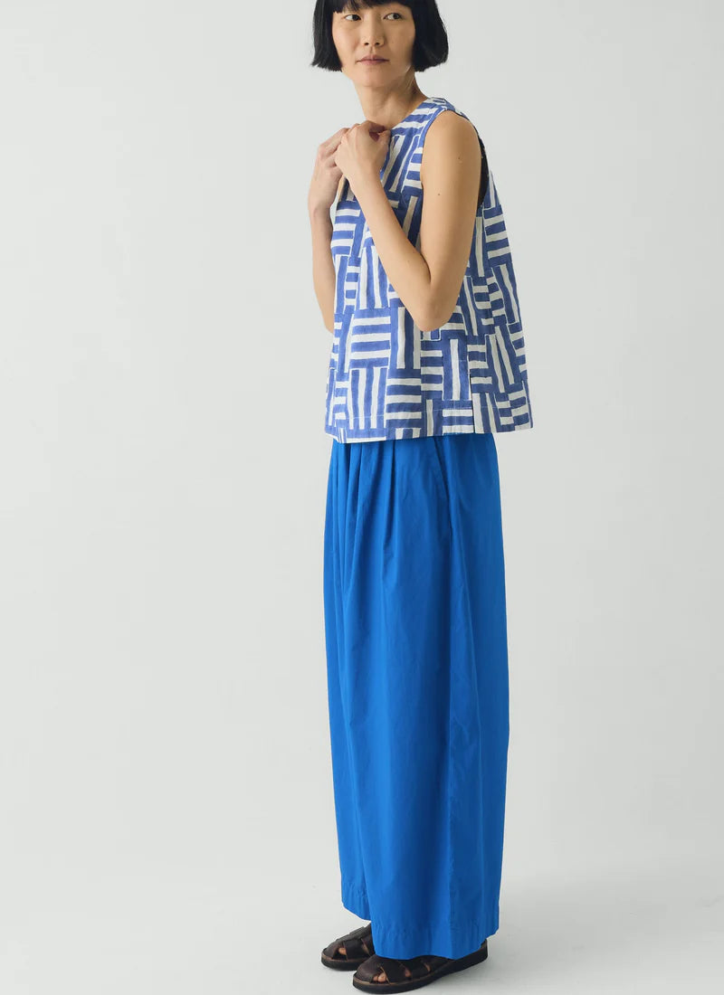 Woman wearing a blue and white patterned sleeveless top with a long blue skirt on a white background