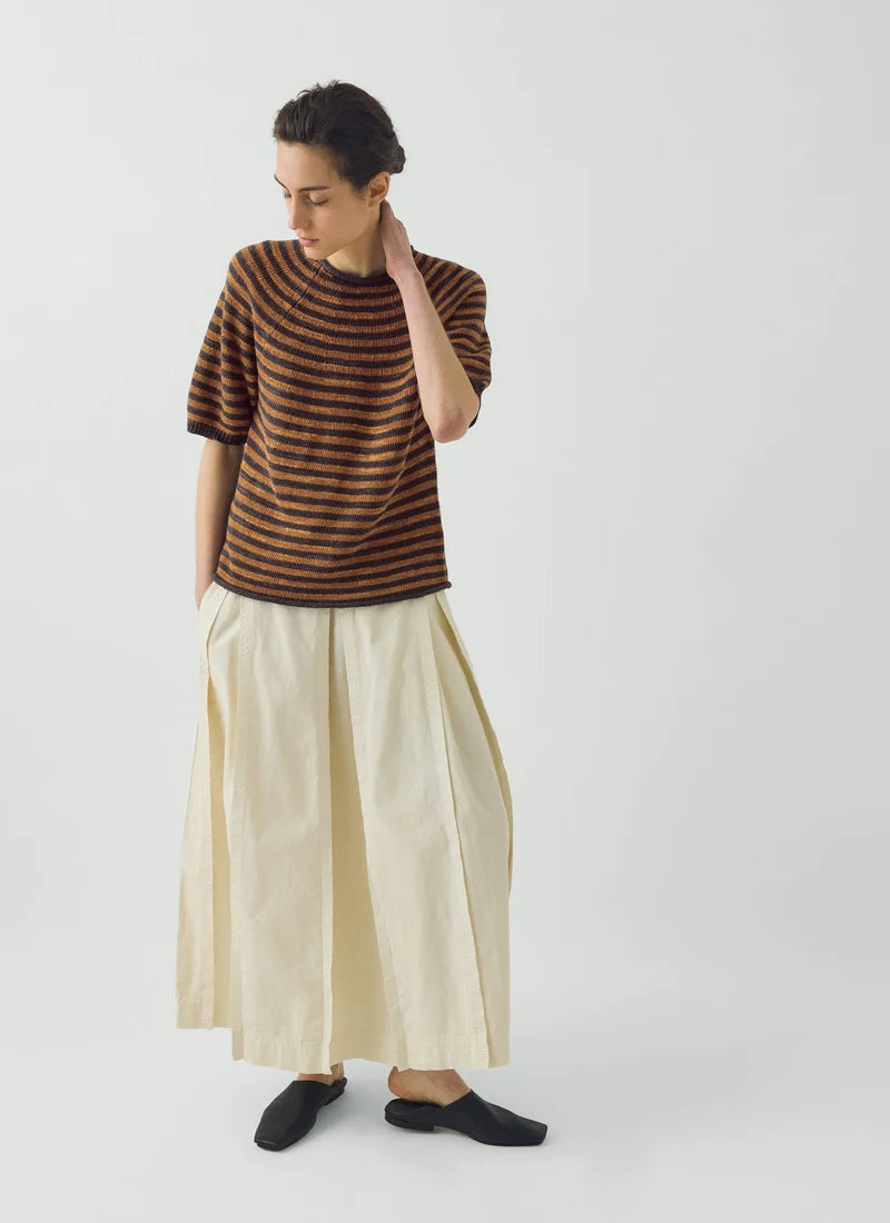 A model shown wearing a soft copper and graphite blue striped knitted and white pants.