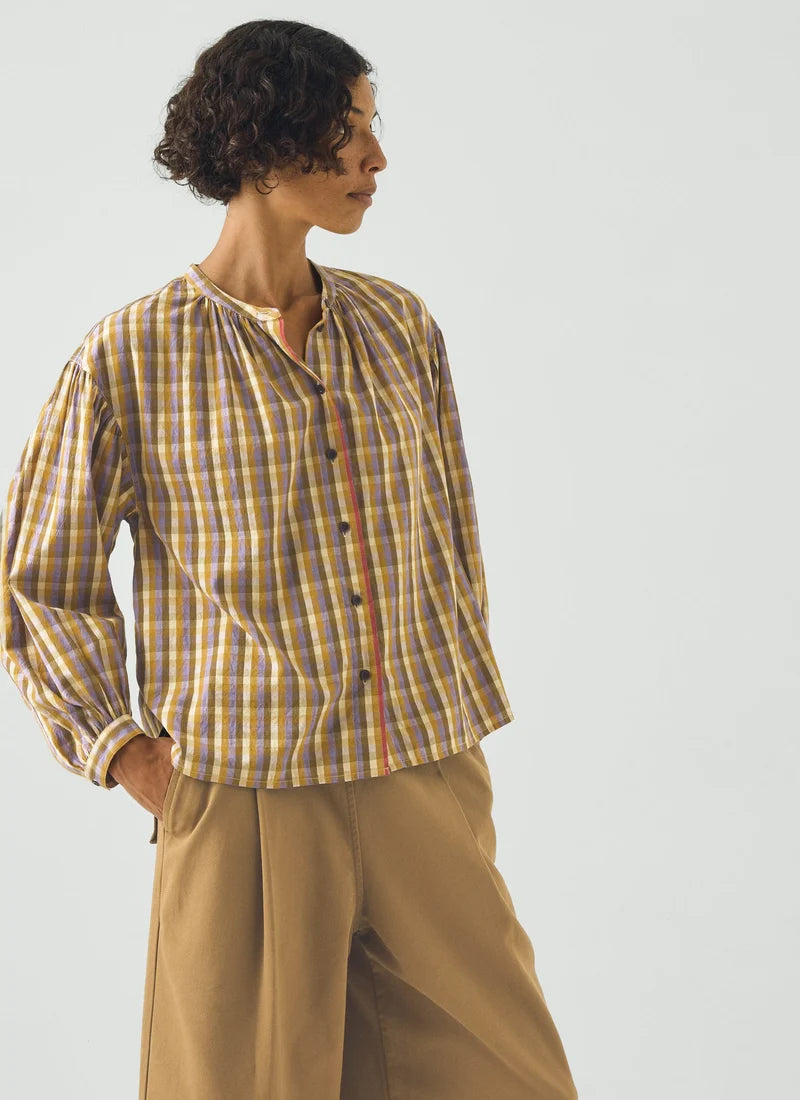 A photo of a model wearing a check top with yellows, greens, and purples.