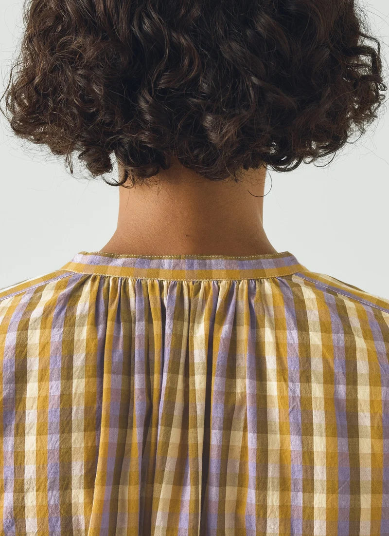 A photo of a model wearing a check top with yellows, greens, and purples.