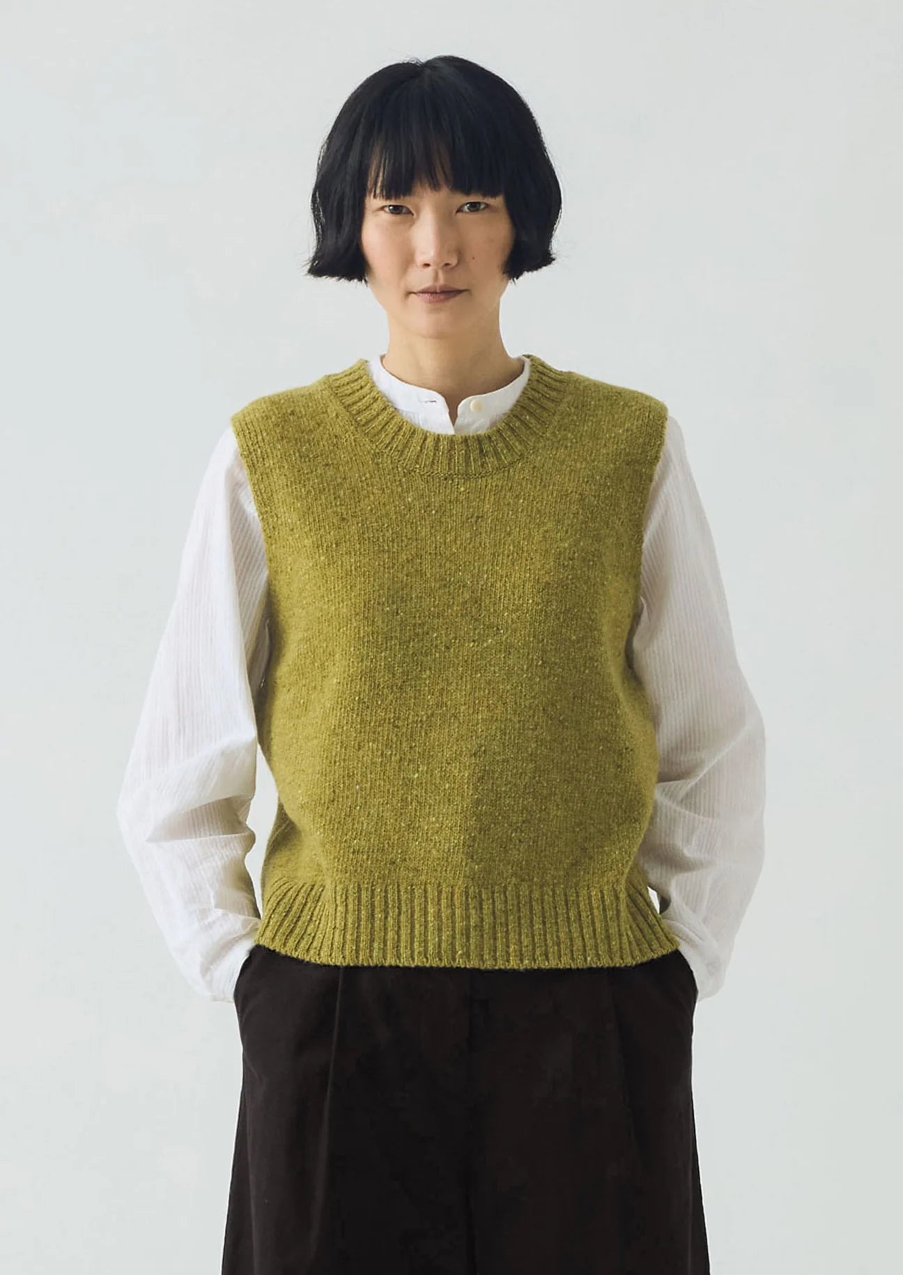 Person wearing a green knitted vest over a white shirt on a plain background