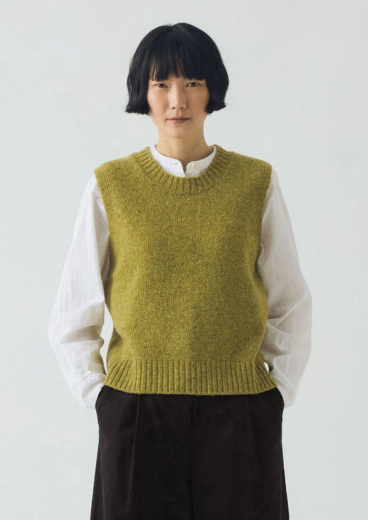 Person wearing a green knitted vest over a white shirt on a plain background