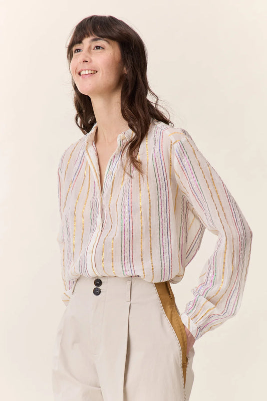 Woman with long brown hair wearing cream colored pants and cream blouse with colorful metalic stripes