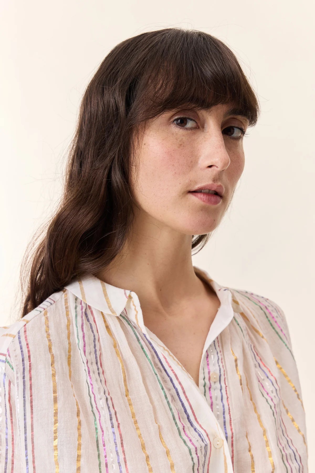 cropped image of Woman with long brown hair wearing cream colored pants and cream blouse with colorful metallic stripes