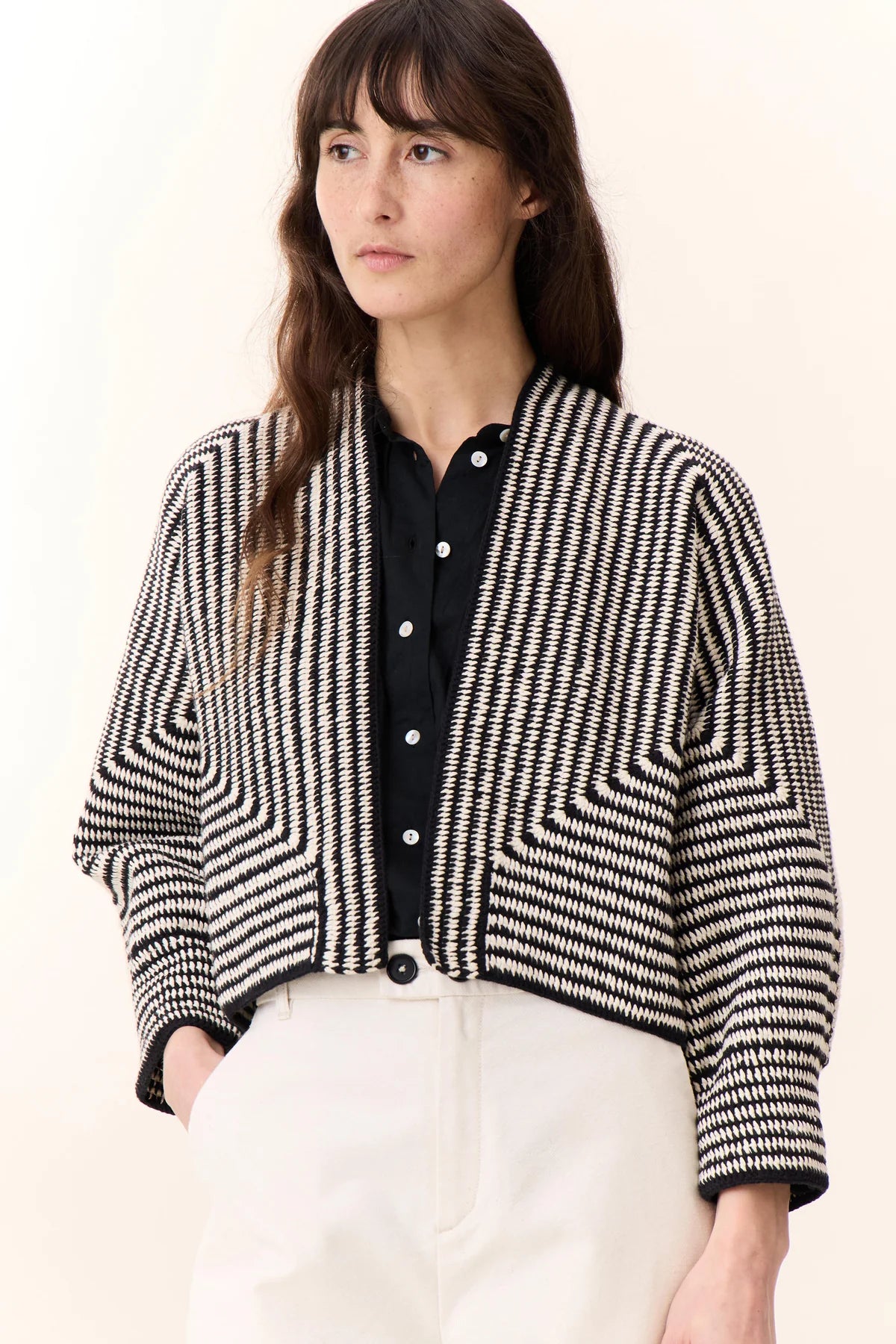 photo of woman with long brown hair wearing white pants, black shirt and black and white striped knit cardigan