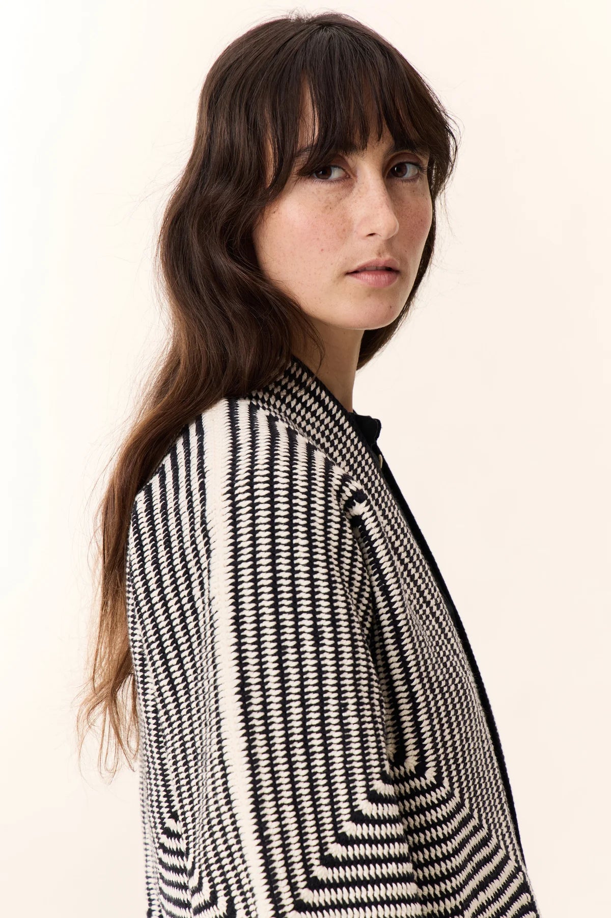 Side view of photo of woman with long brown hair wearing white pants, black shirt and black and white striped knit cardigan