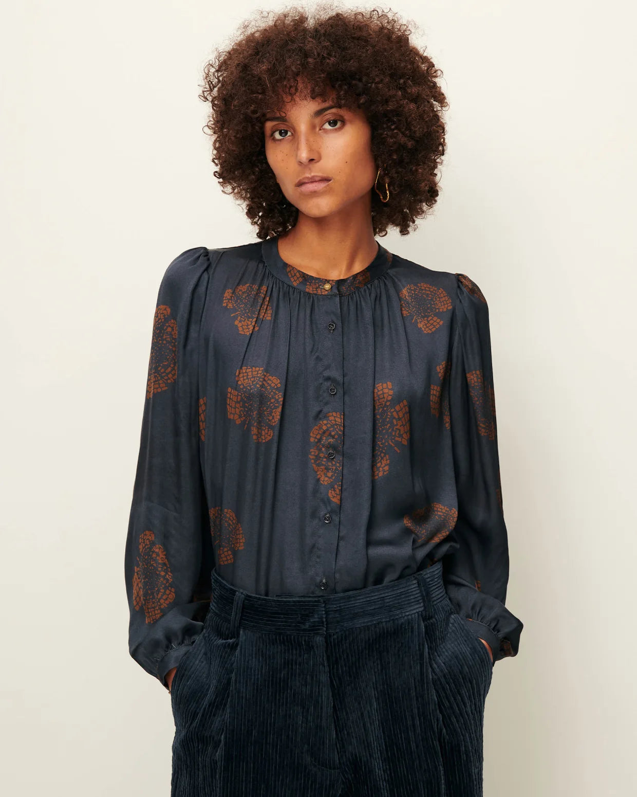 Woman wearing a dark blue blouse with floral patterns against a plain background