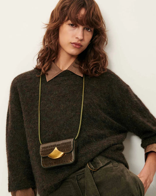 Woman wearing a dark brown sweater with a gold necklace and a small brown bag.