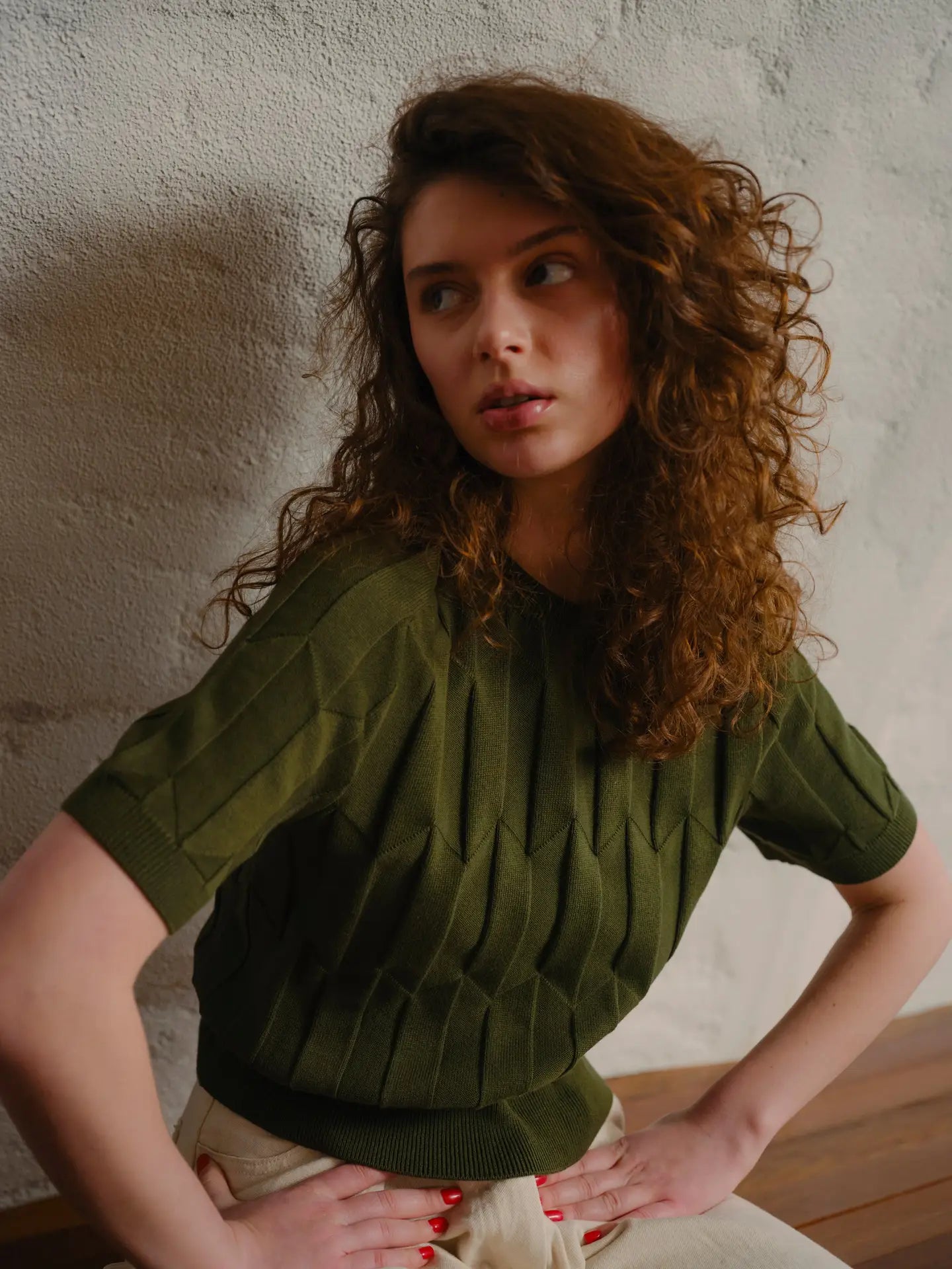 Woman wearing a green sweater against a textured wall.