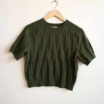 An olive green short-sleeve knit top with a textured vertical ribbed pattern, hanging on a wooden hanger against a plain white wall.