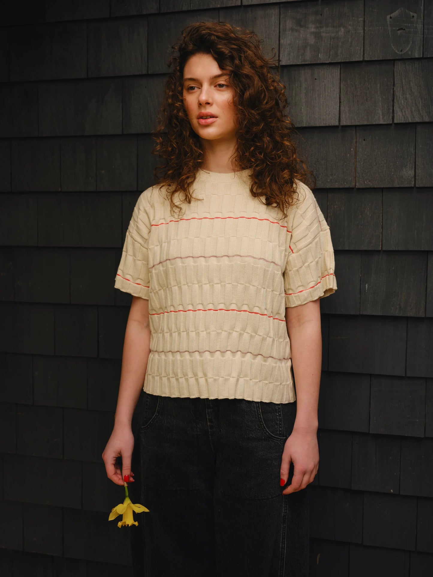 Woman wearing a beige textured shirt against a dark wooden wall