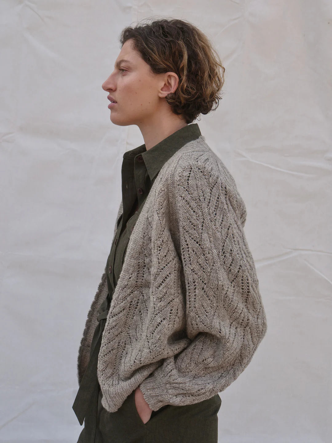 Side view of woman wearing a beige knitted cardigan against a plain background