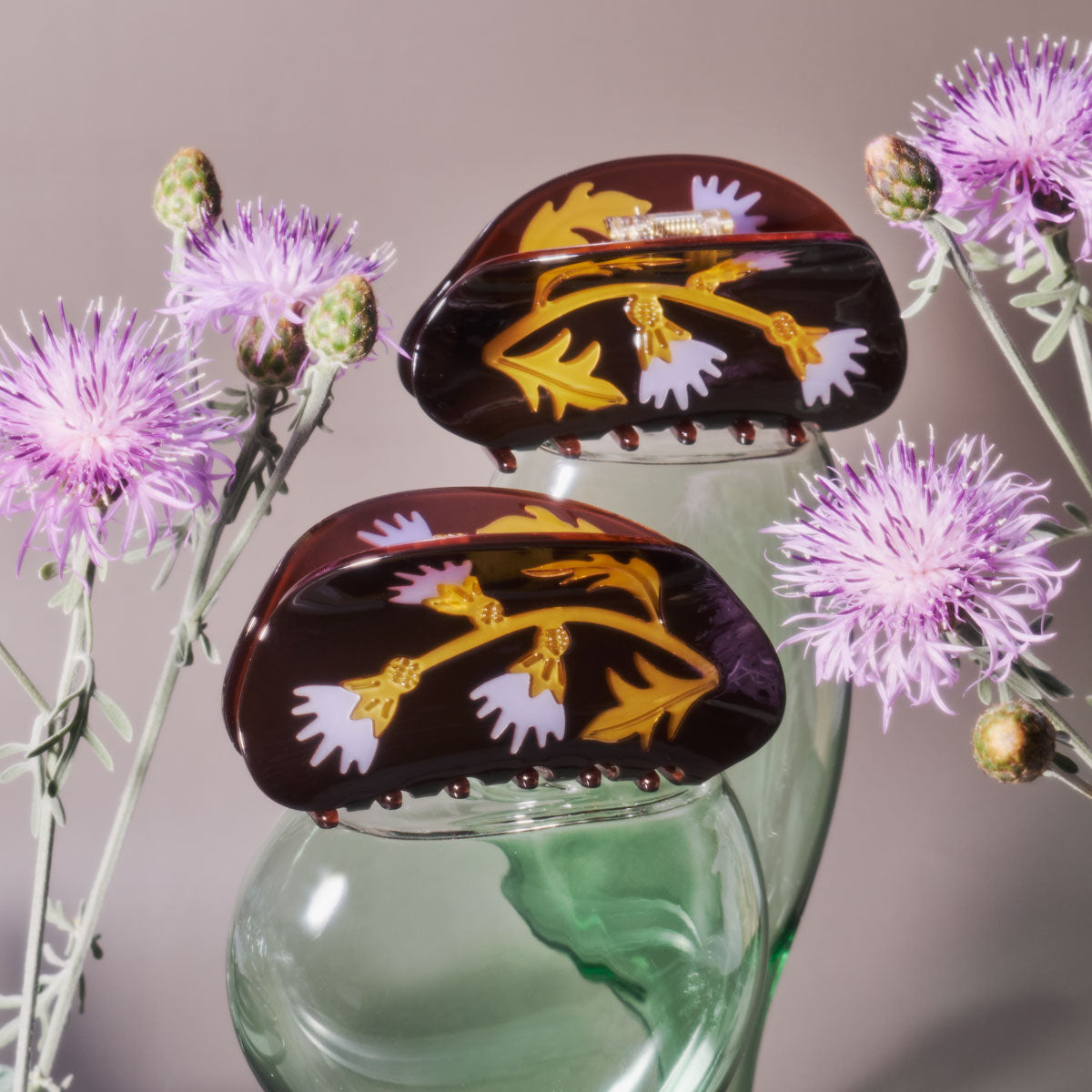 Floral design hair claws on a glass stand with purple flowers in the background.