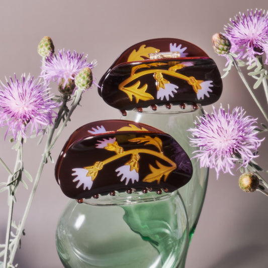 Floral design hair claws on a glass stand with purple flowers in the background.