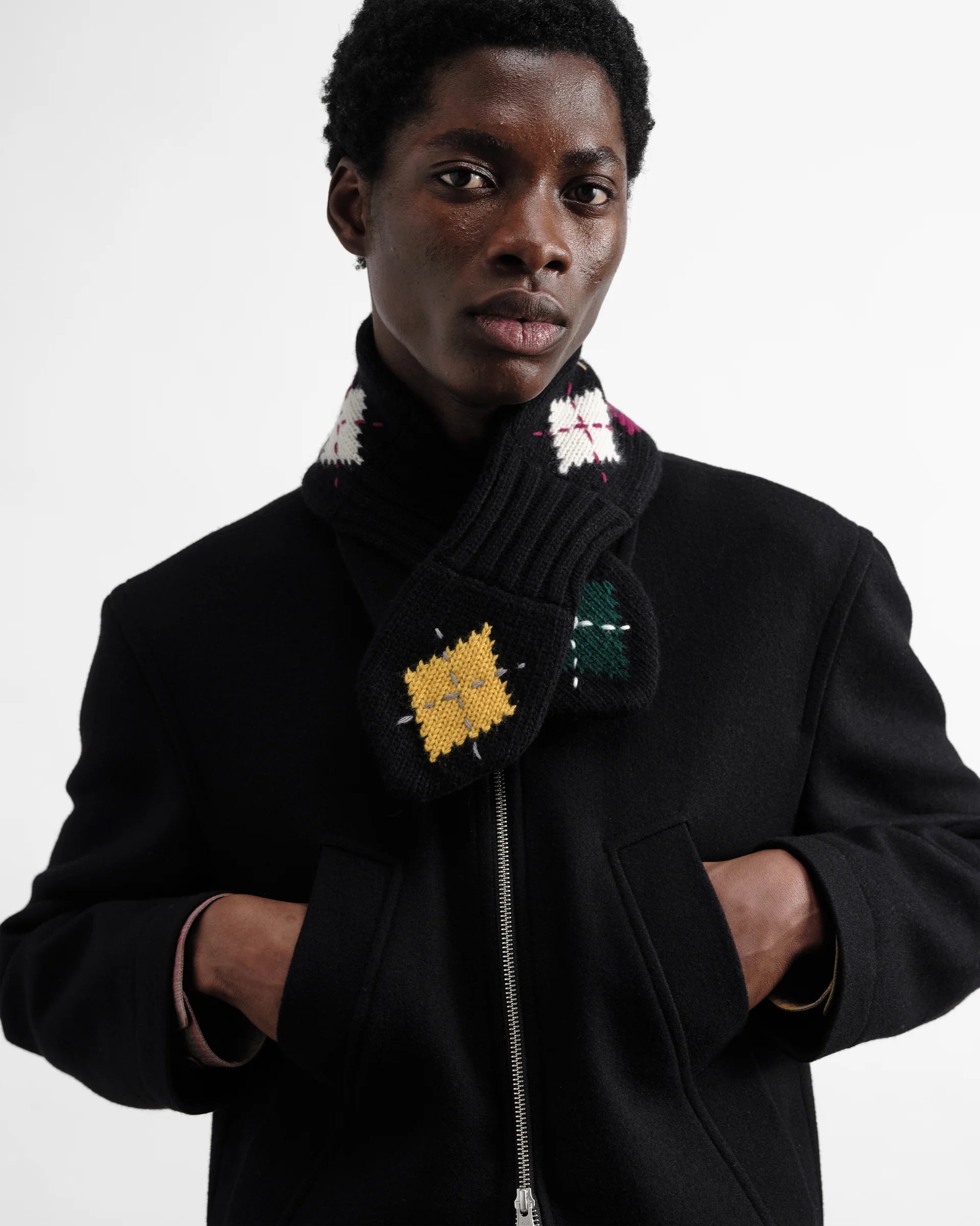 Person wearing a black coat with Wiith argyle scarf on a white background