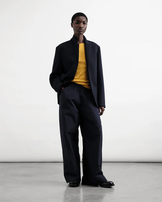 Person wearing a navy Jacket  and pants with a yellow shirt against a white background
