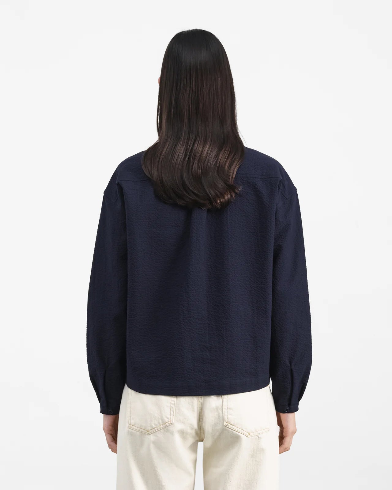 Person wearing a navy blue sweater and light-colored pants on a white background