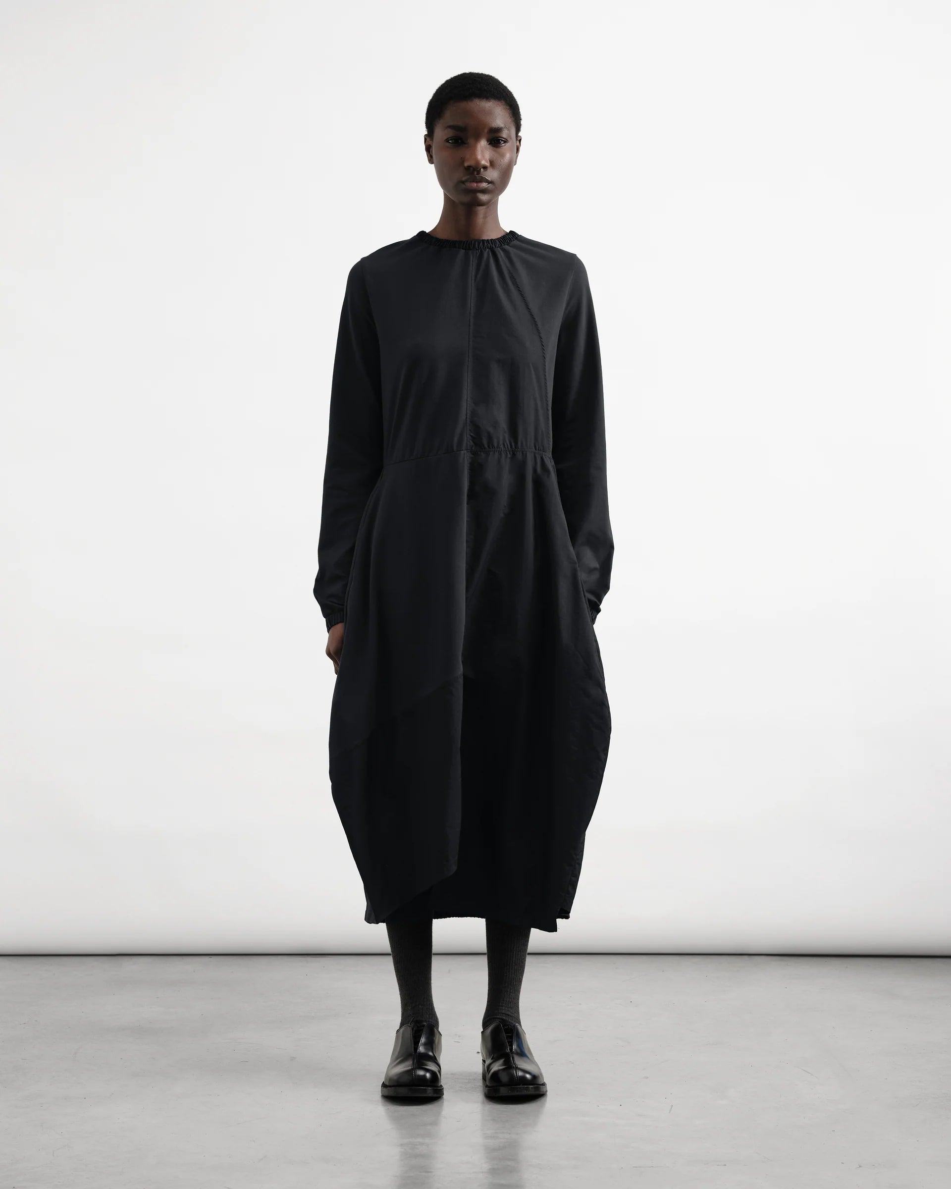 Person wearing a black dress standing against a white background