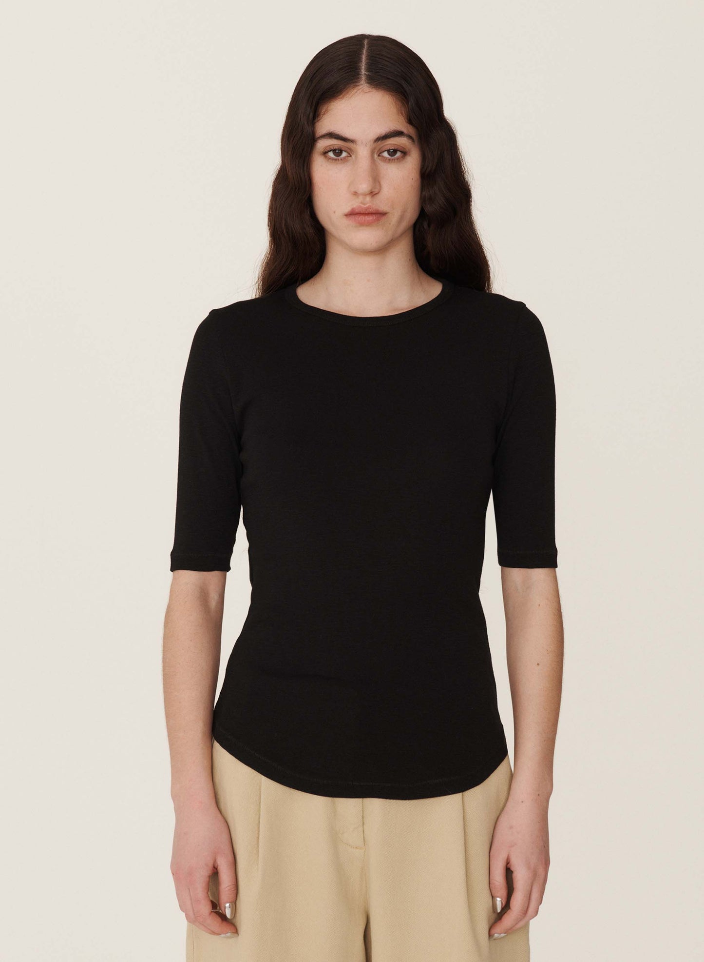 Black crew neck t-shirt. Elbow length sleeves and curved hem. worn over pleated beige pants