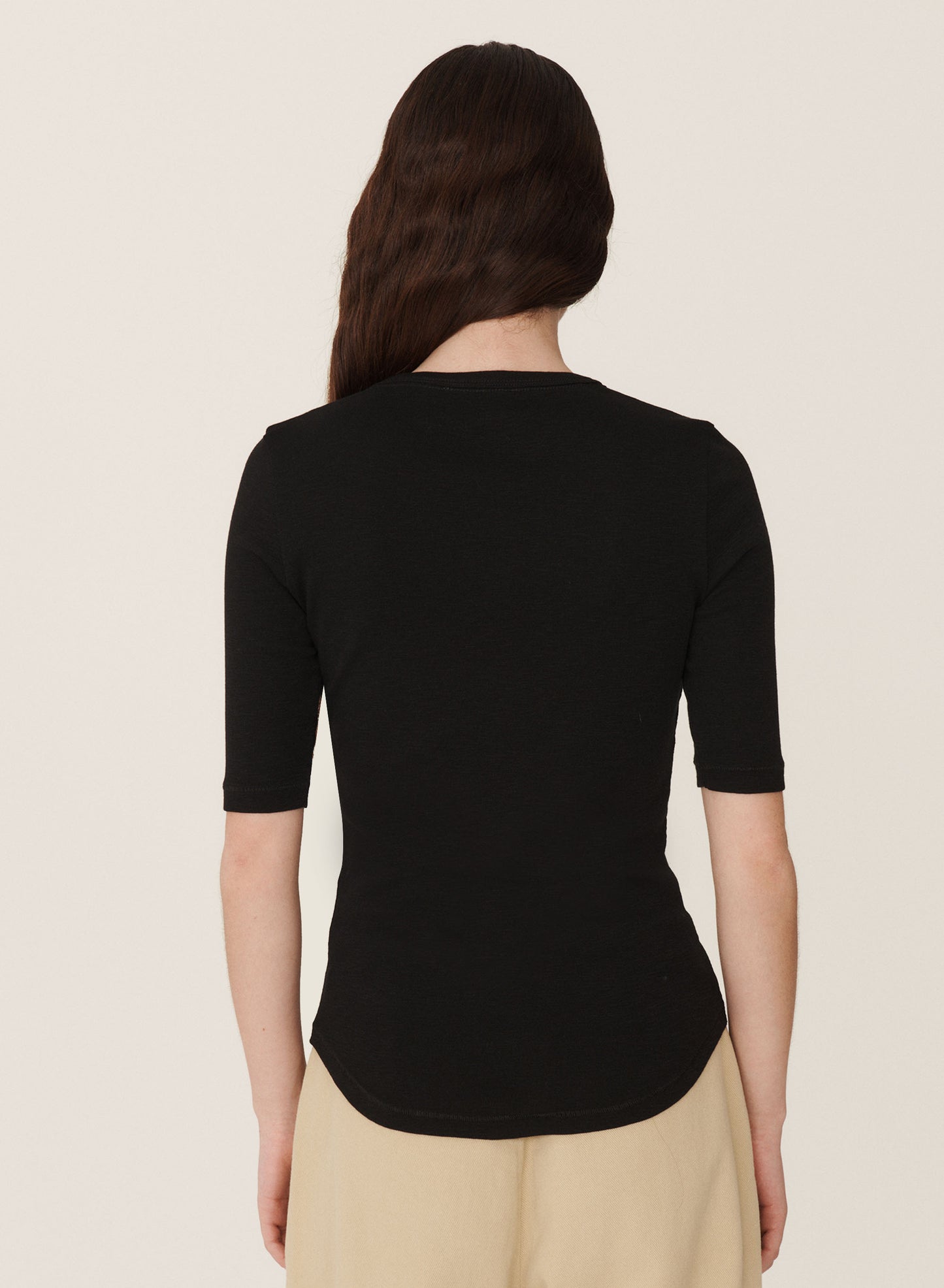 Back view of black crew neck t-shirt. worn over the waist of beige pants